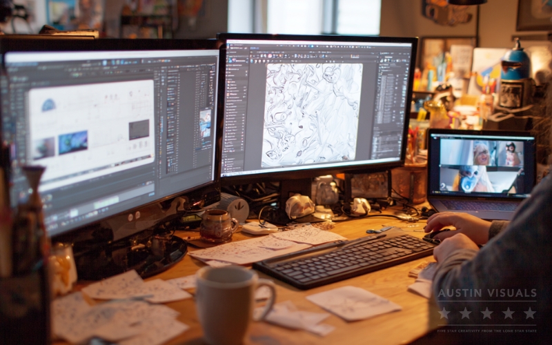 Why Customer Consultation Defines Successful Corporate Video Production 3 animation artist working at dual monitors creating d and d assets desk covered with sketches and coffee mug video call on laptop in background austin visuals studio