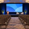 Two cameras positioned to record a fictional corporate conference stage
