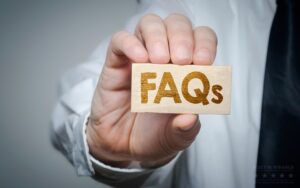 Person in business attire holding a small wooden block with the word FAQs engraved in bold gold letters