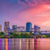 View of downtown Little Rock Arkansas featuring the illuminated bridge reflecting on the calm river under a vibrant sunset sky Austin Visuals logo displayed